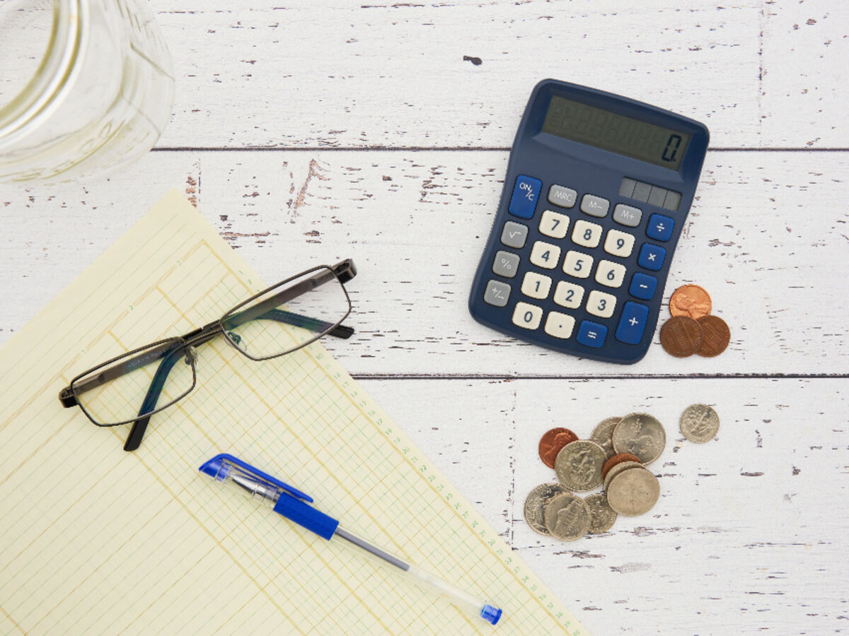 A calculator, glasses, and coins laid out on a notepad for accounting work